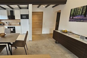 A modern kitchen with a dining area, a wooden door, and a wall-mounted artwork.