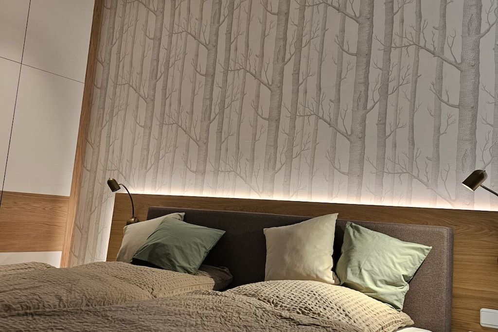 Une chambre à coucher avec un lit, des oreillers et un mur décoré d’un motif d’arbre.