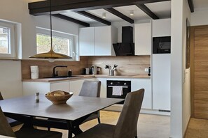 Une cuisine moderne avec des meubles blancs, un plan de travail en bois et un coin repas comprenant une table et des chaises.