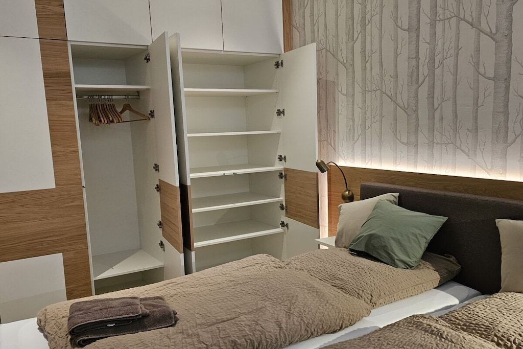 A bedroom with a bed, a nightstand, a wardrobe, and a wall with a tree pattern.
