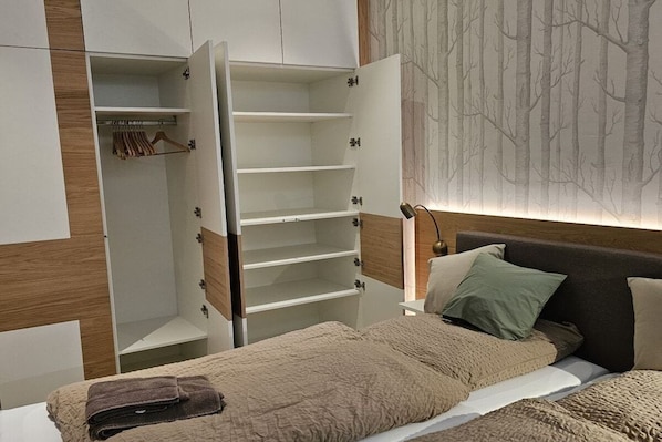 A bedroom with a bed, a nightstand, a wardrobe, and a wall with a tree pattern.