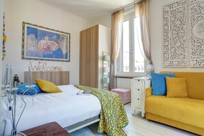 Una habitación de hotel con cama, escritorio, sofá y ventana con cortinas.