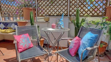Un patio con dos sillas de metal, una mesa redonda pequeña y plantas en macetas.