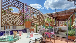 En udendørs patio med et spisebord, omgivet af krukker med planter og en trækonstruktion.