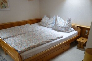 Una cama individual con estructura de madera, colchón blanco y ropa de cama estampada con motivos florales.