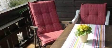 A wooden deck with a table and chairs, a potted plant, and a view of trees.
