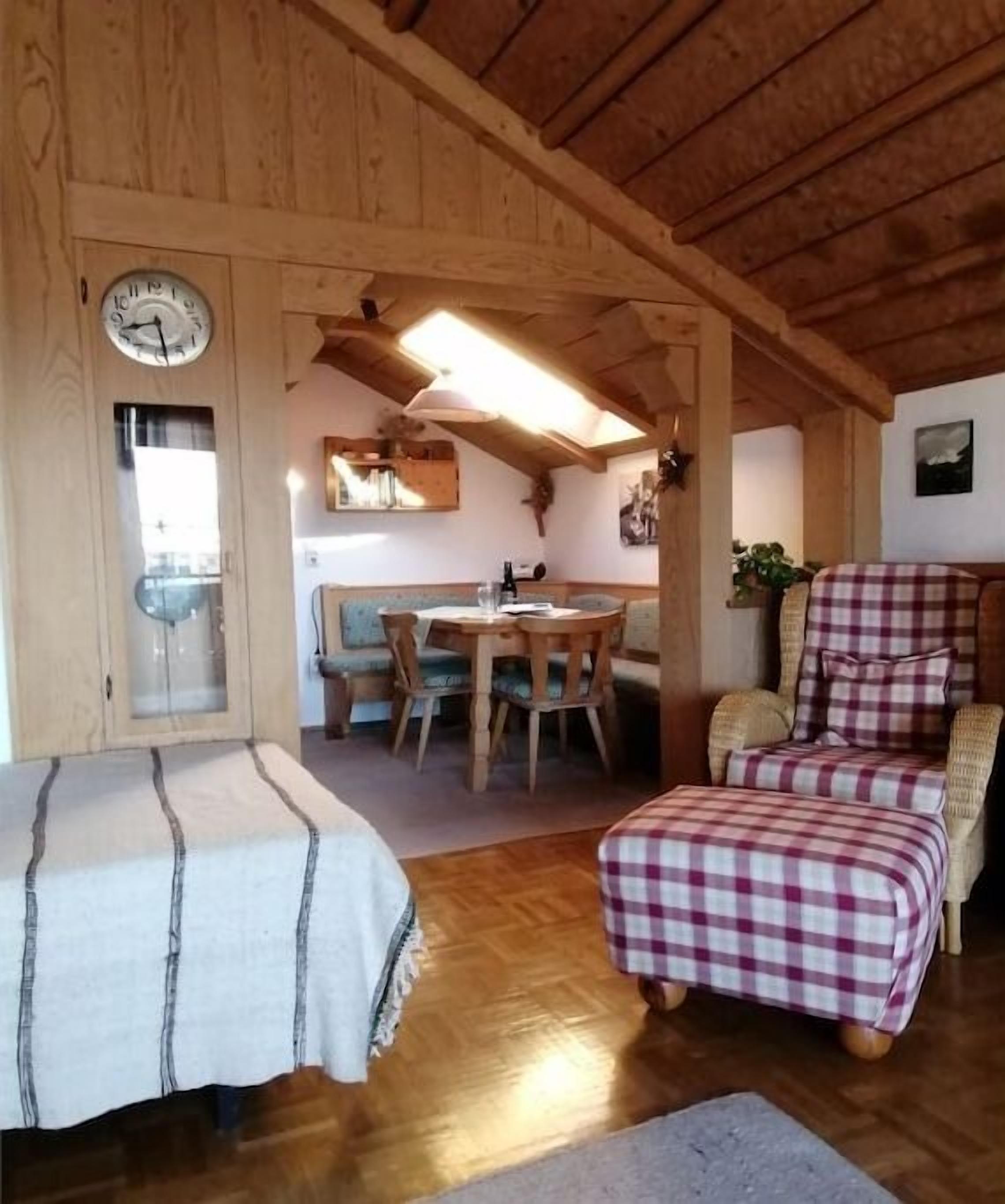 A cozy room with a wooden ceiling, a dining table with chairs, a checkered sofa, and a clock on the wall.