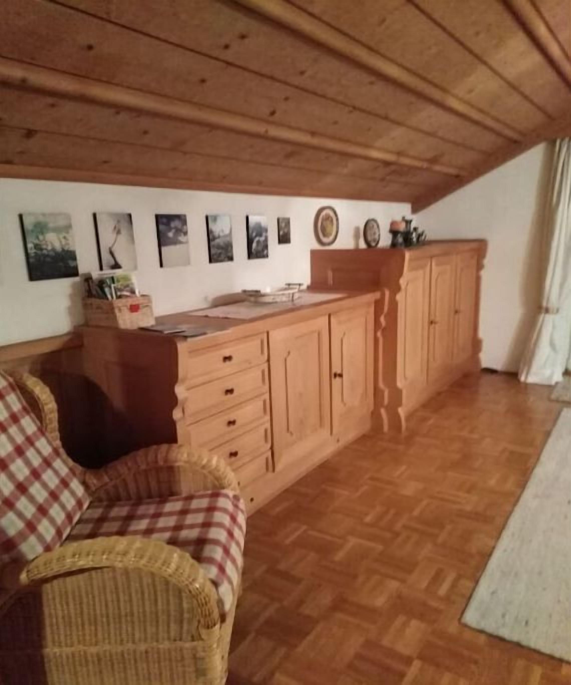 A room with a wooden ceiling, a wooden cabinet, a wicker sofa, and a wooden floor.