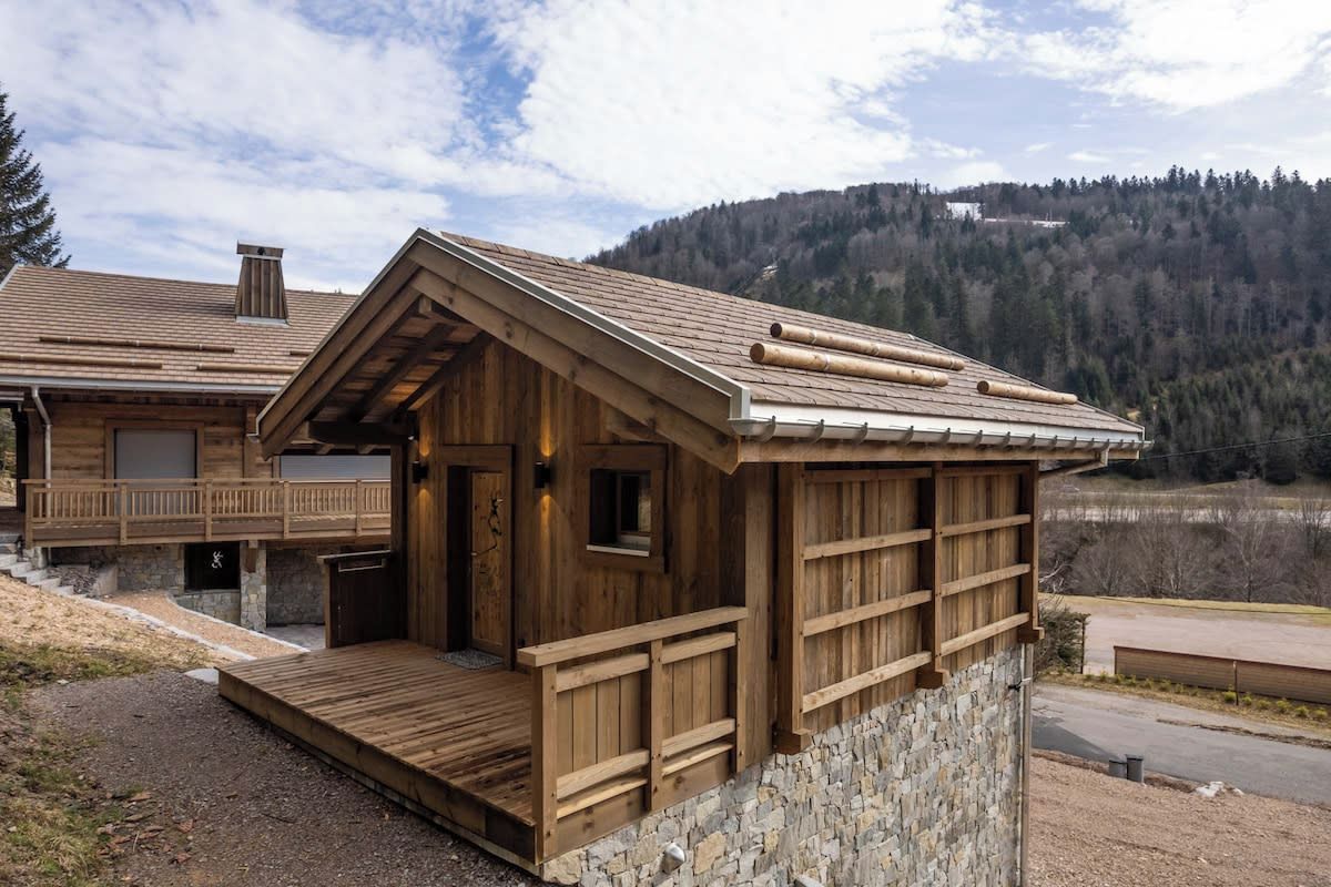 Une cabane en bois avec des fondations en pierre, une véranda couverte et une vue sur une colline boisée.