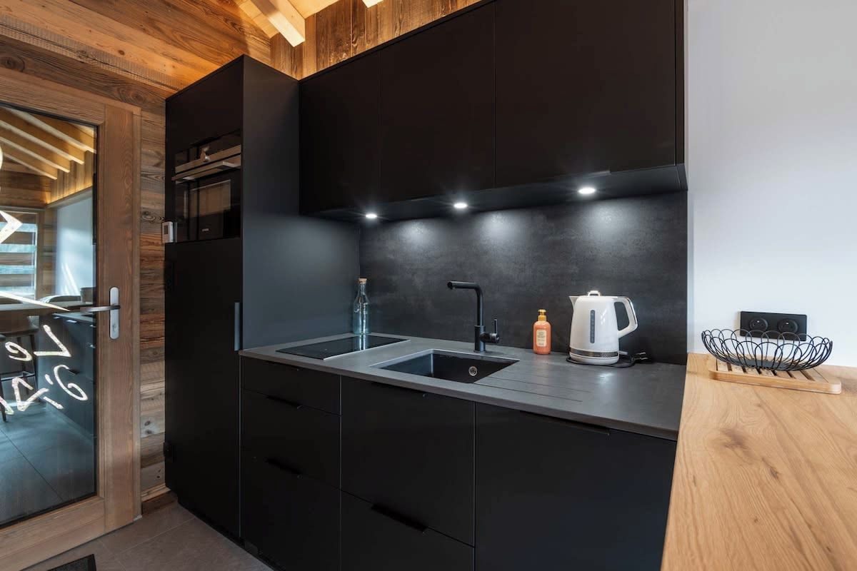 A modern kitchen with black cabinetry, a stainless steel sink, and a kettle on the countertop.