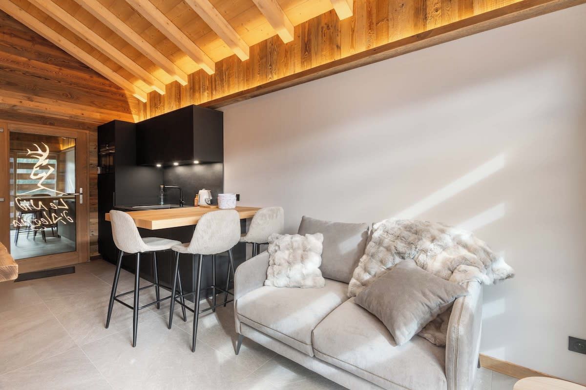 A modern interior with a wooden ceiling, a kitchen area, a dining table with chairs, and a sofa with decorative pillows.