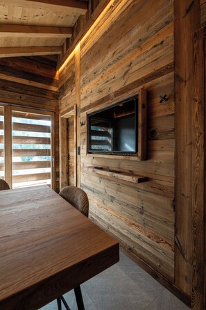 A wooden interior with a flat-screen TV mounted on a wall, a dining table, and a chair. - ✨ Le Nid d'Alegria – Luxury Mountain Retreat at the Foot of the Slopes (La Bresse)