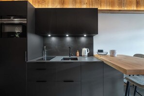 A modern kitchen with a dark countertop, a wooden dining table, and a built-in oven. - ✨ Le Nid d'Alegria – Luxury Mountain Retreat at the Foot of the Slopes (La Bresse)