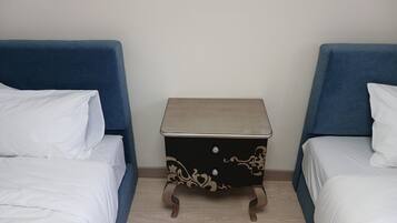 A room with two beds, each with white bedding, and a small bedside table with a decorative design.