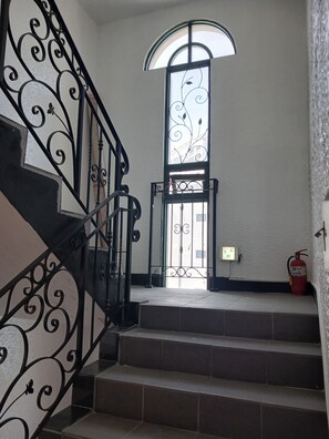 Una escalera con barandillas de metal ornamentadas que conduce a una puerta con un panel de vidrio decorativo.