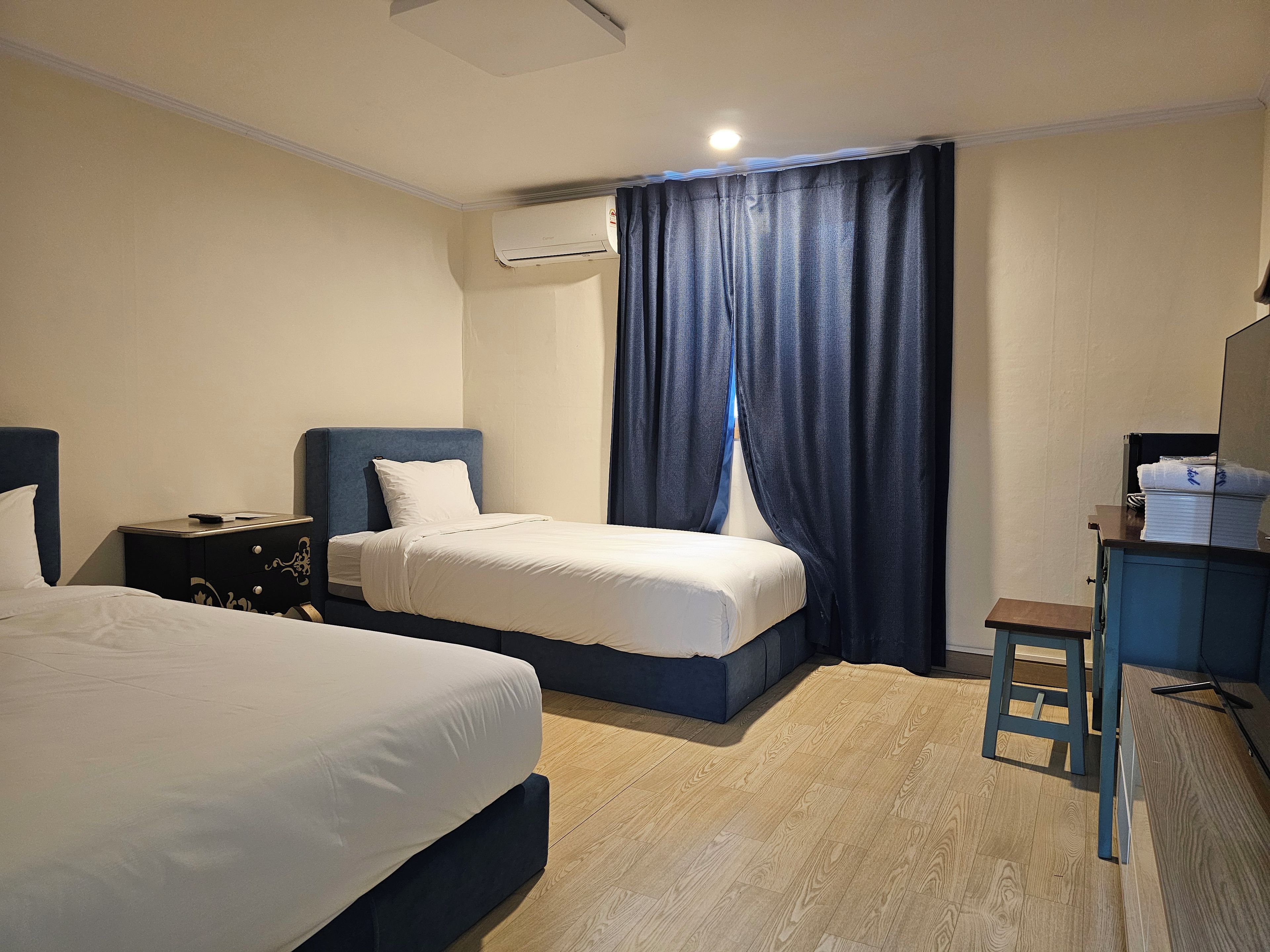 A hotel room with two beds, a desk, a chair, an air conditioning unit, and a curtain.