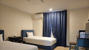 Una camera d'albergo con due letti, una scrivania, una sedia, un condizionatore d'aria e una tenda.