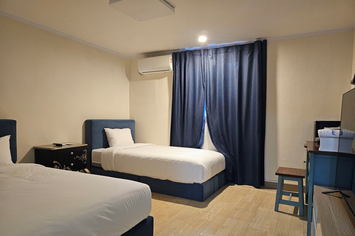 A hotel room with two beds, a desk, a chair, an air conditioning unit, and a curtain.