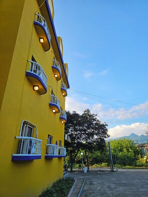 Un edificio amarillo con varios balcones, cielo despejado y una cadena montañosa distante.