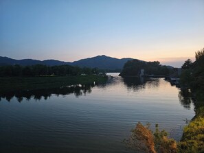 A calm river with a bridge, surrounded by trees and hills.