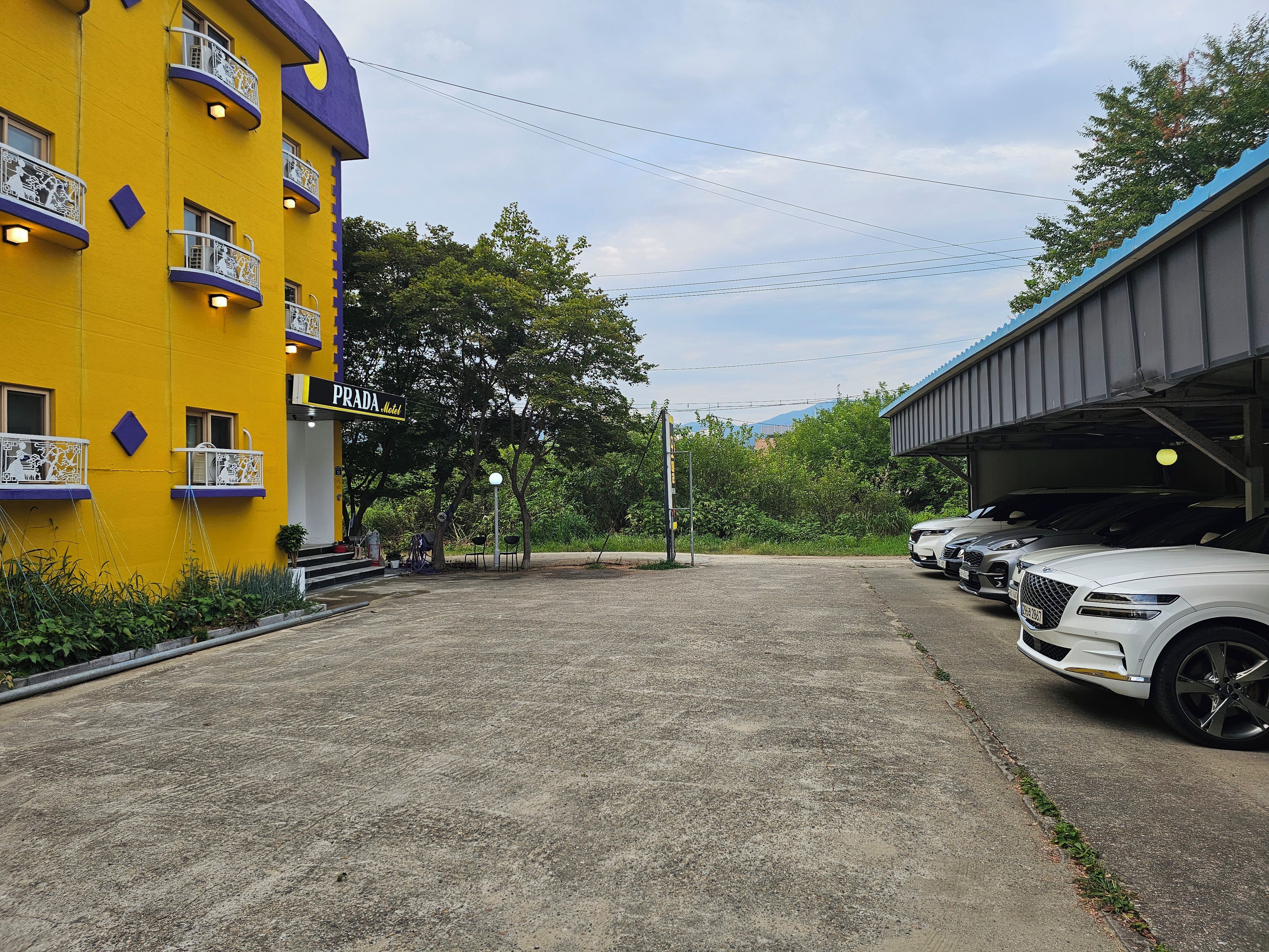 A hotel with a yellow facade, outdoor seating, and a parking area with several cars.
