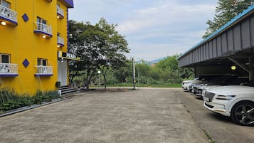 A hotel with a yellow facade, outdoor seating, and a parking area with several cars.