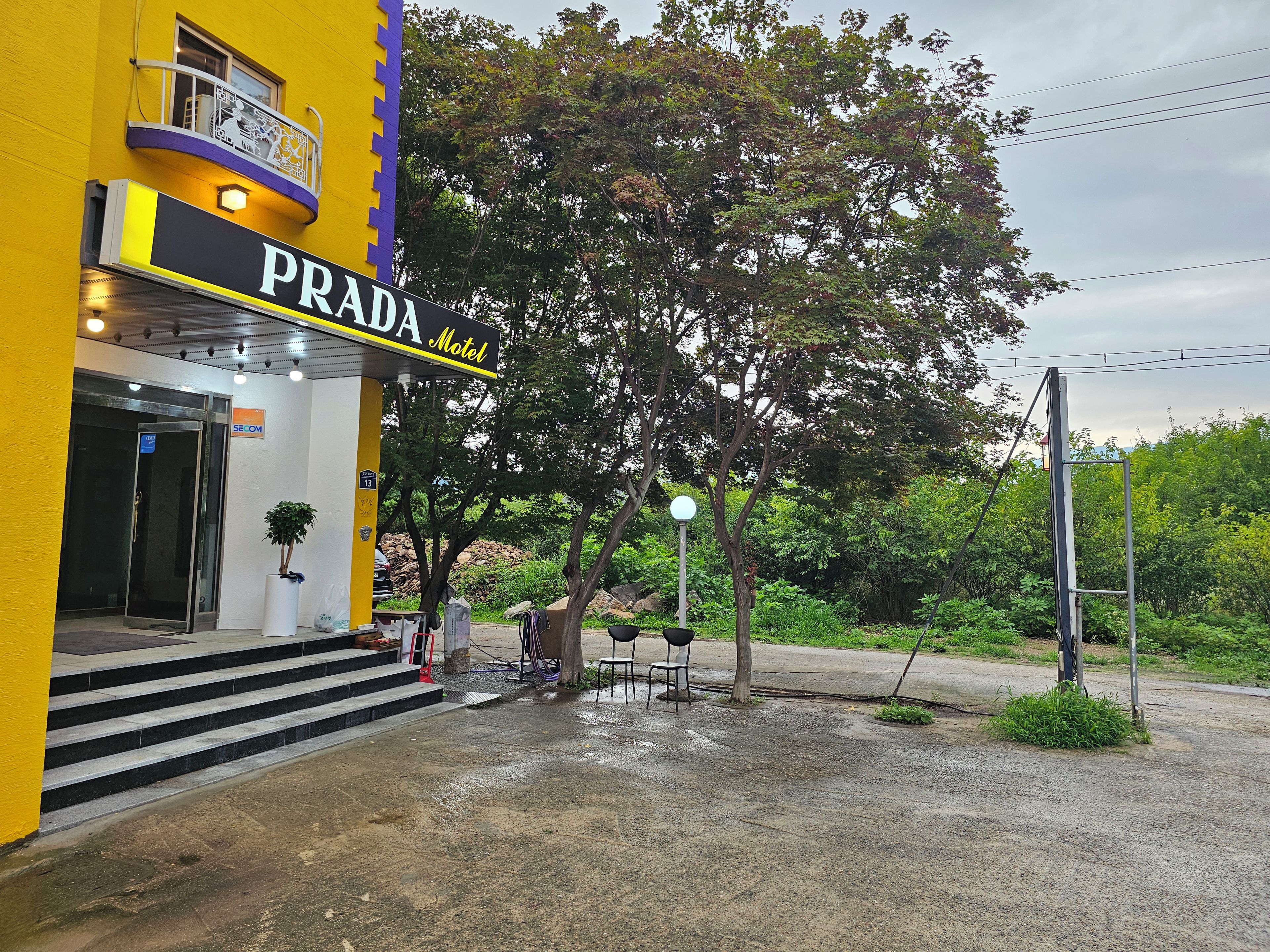 Un motel PRADA con fachada amarilla, entrada visible y escaleras que llevan a la puerta.