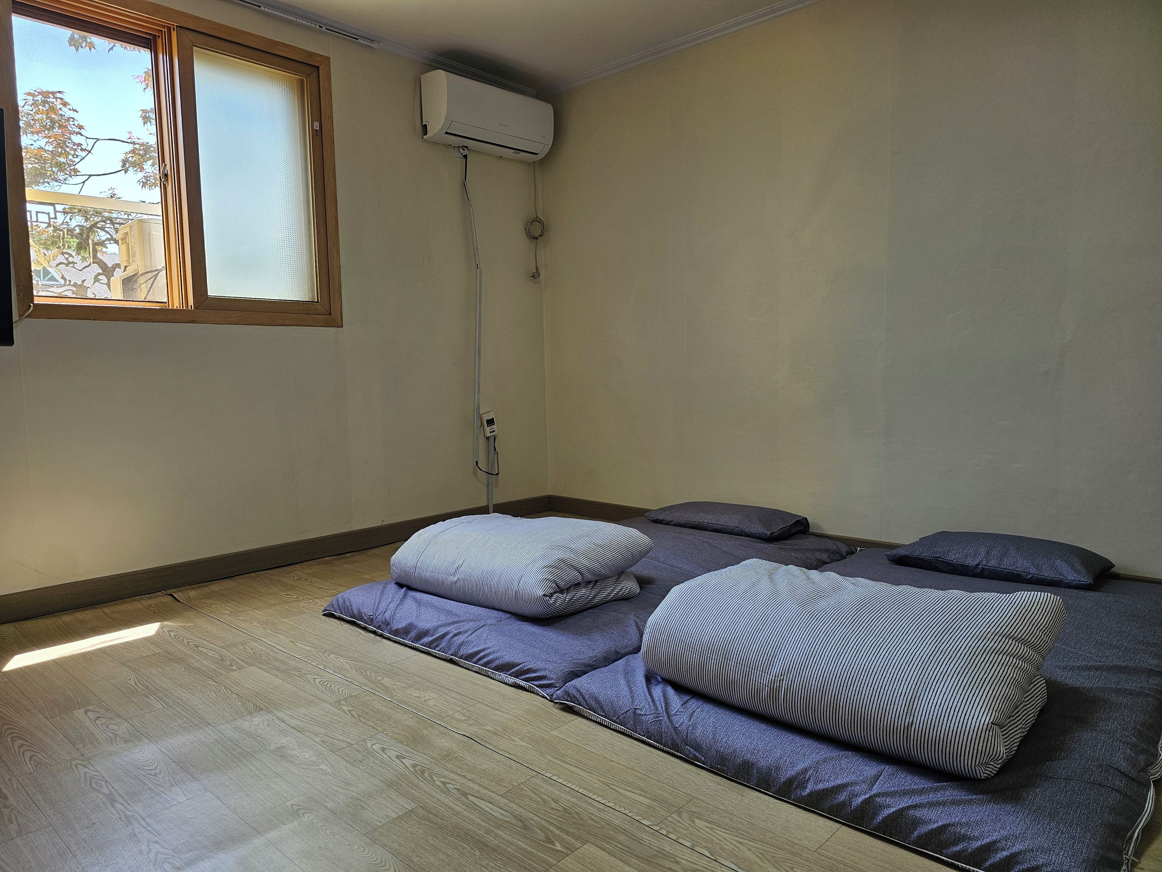 Una habitación con una cama, almohadas, una ventana y un equipo de aire acondicionado.