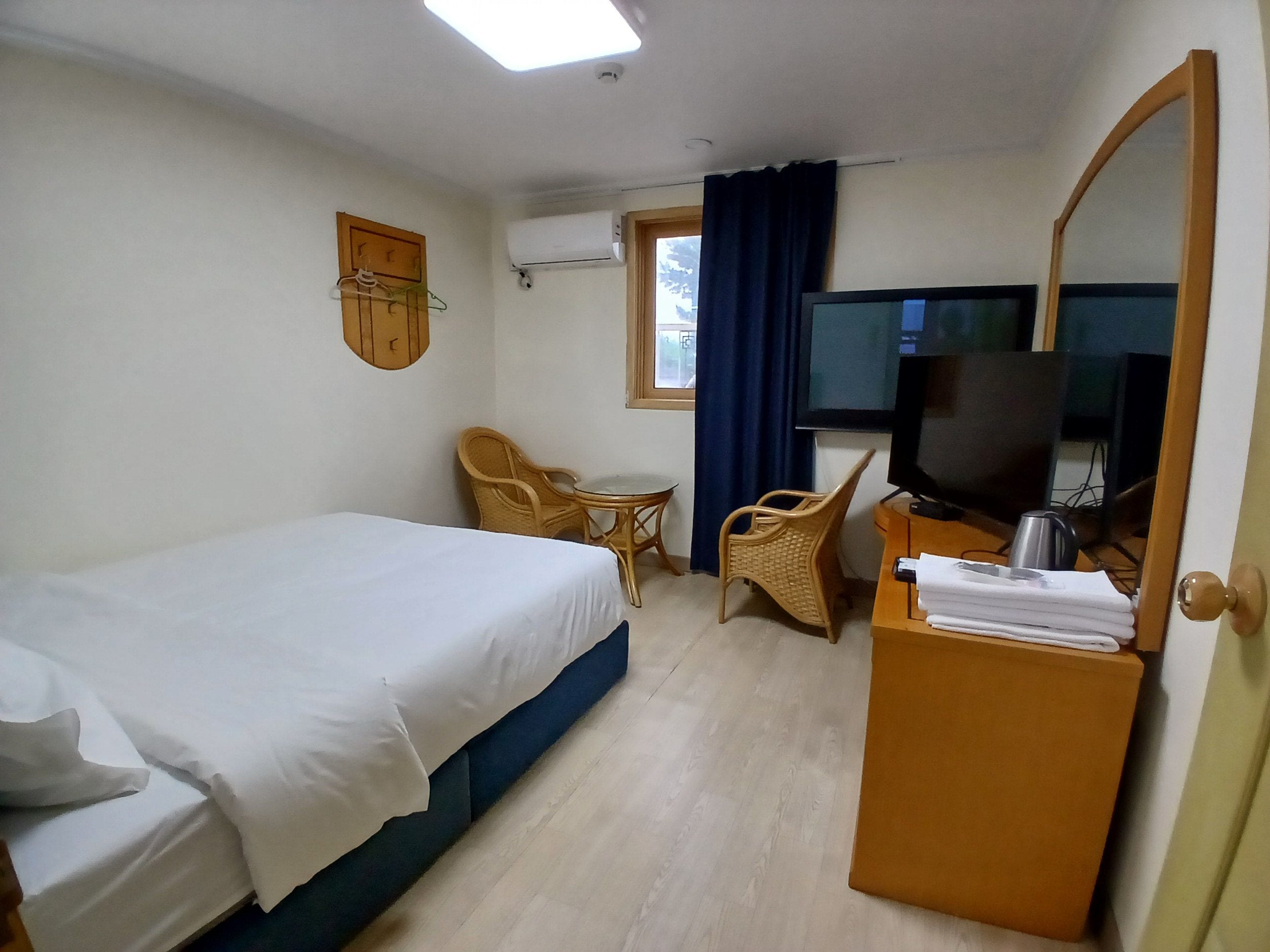 A hotel room with a bed, a television, a desk with a chair, and a window with curtains.