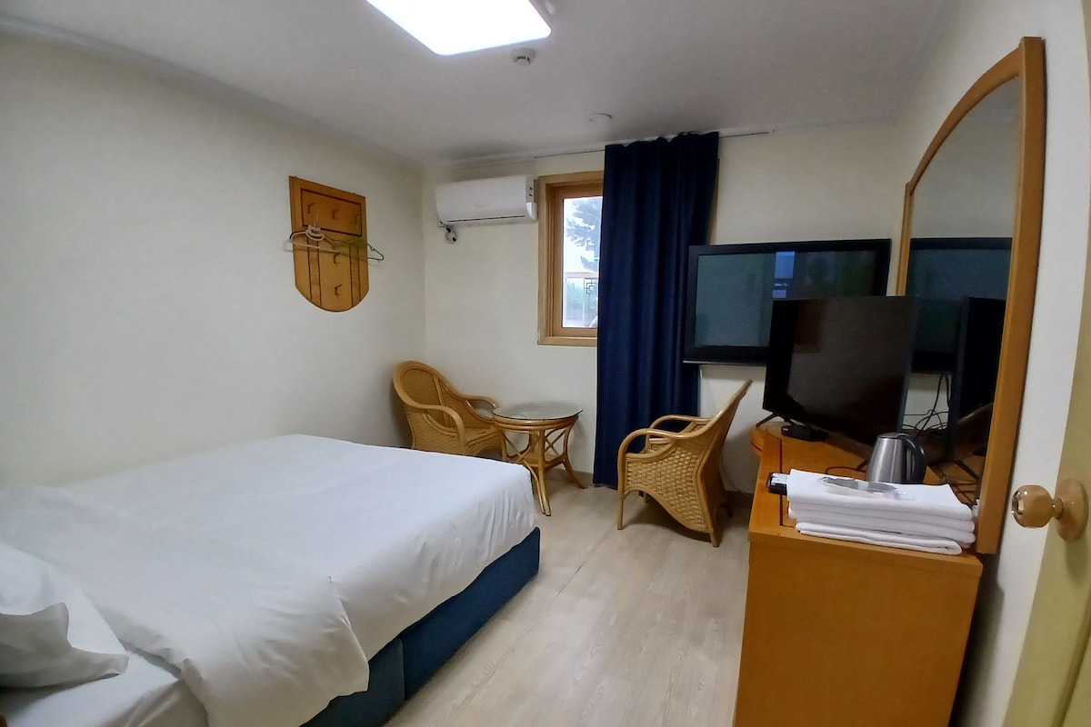 A hotel room with a bed, a television, a desk with a chair, and a window with curtains.