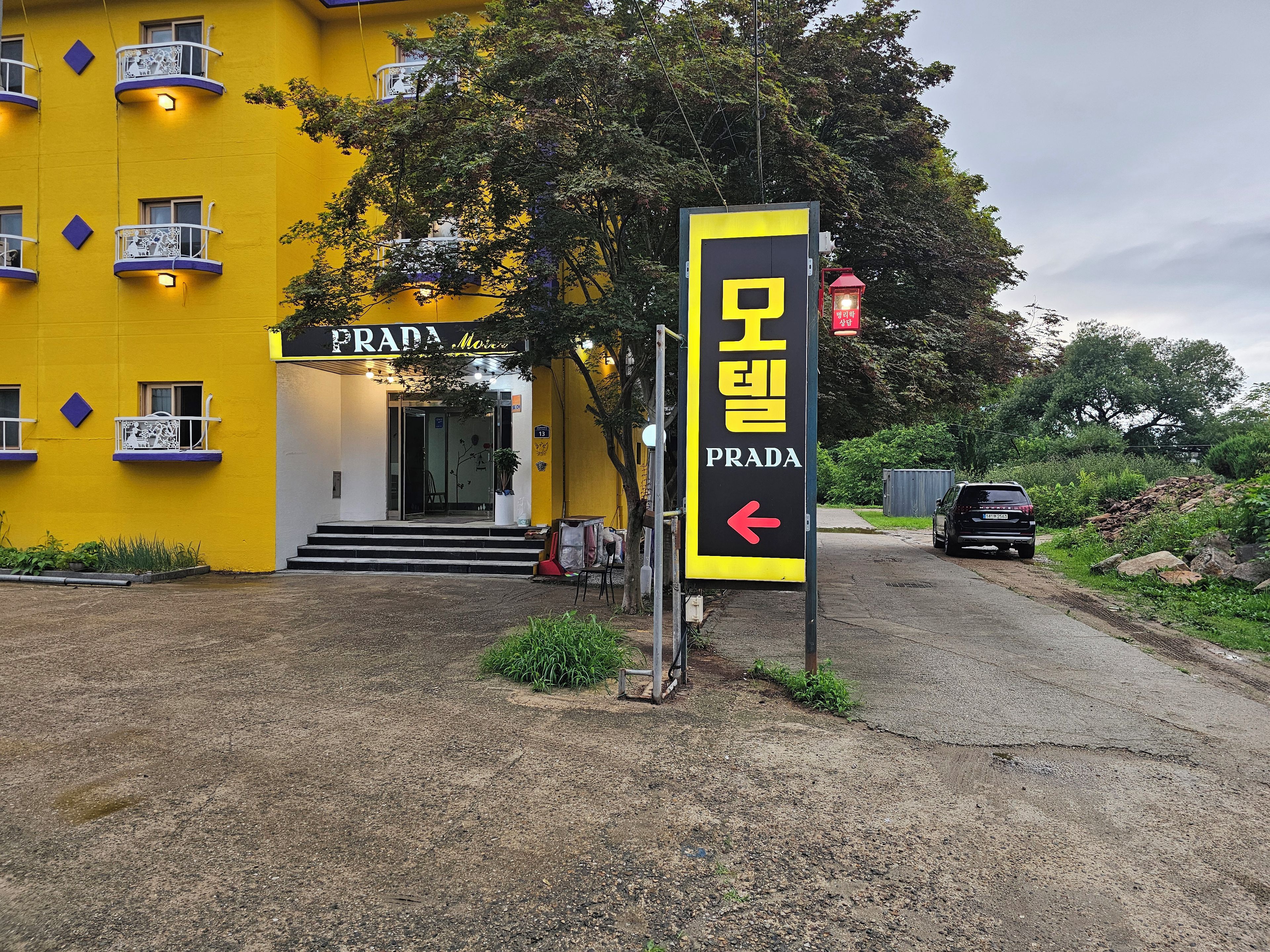 En gul byggnad med en skylt som visar ordet ”PRADA” och en vägvisningsskylt som pekar åt vänster.