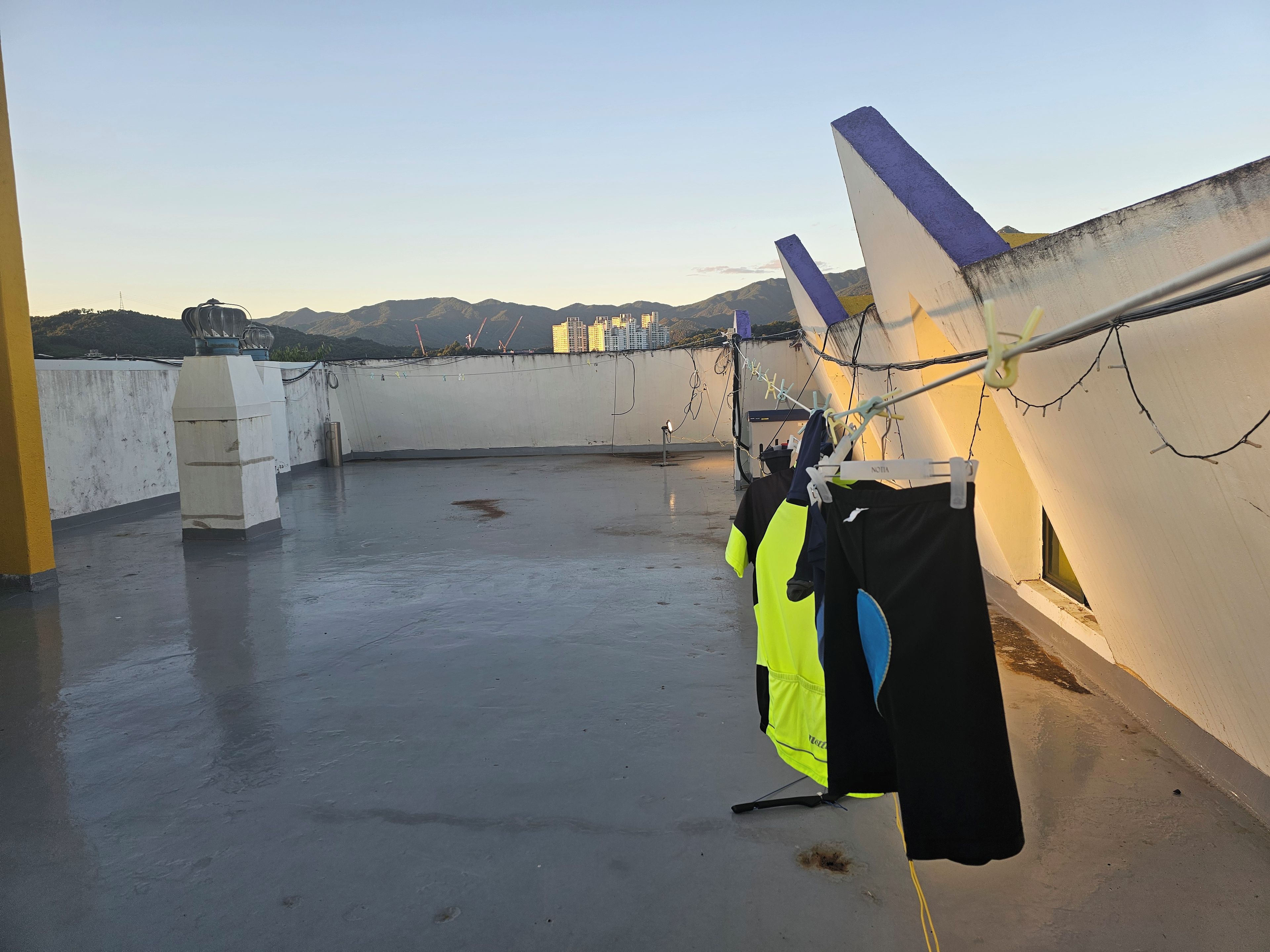 A rooftop with a concrete floor, a clothesline with garments, and a view of distant mountains.