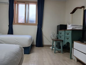 A bedroom with two beds, a desk with drawers, a fan, and a window with curtains.