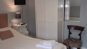 Een slaapkamer met een bed, een kledingkast, een stoel, een nachtkastje, een lamp, een televisie en een spiegel.