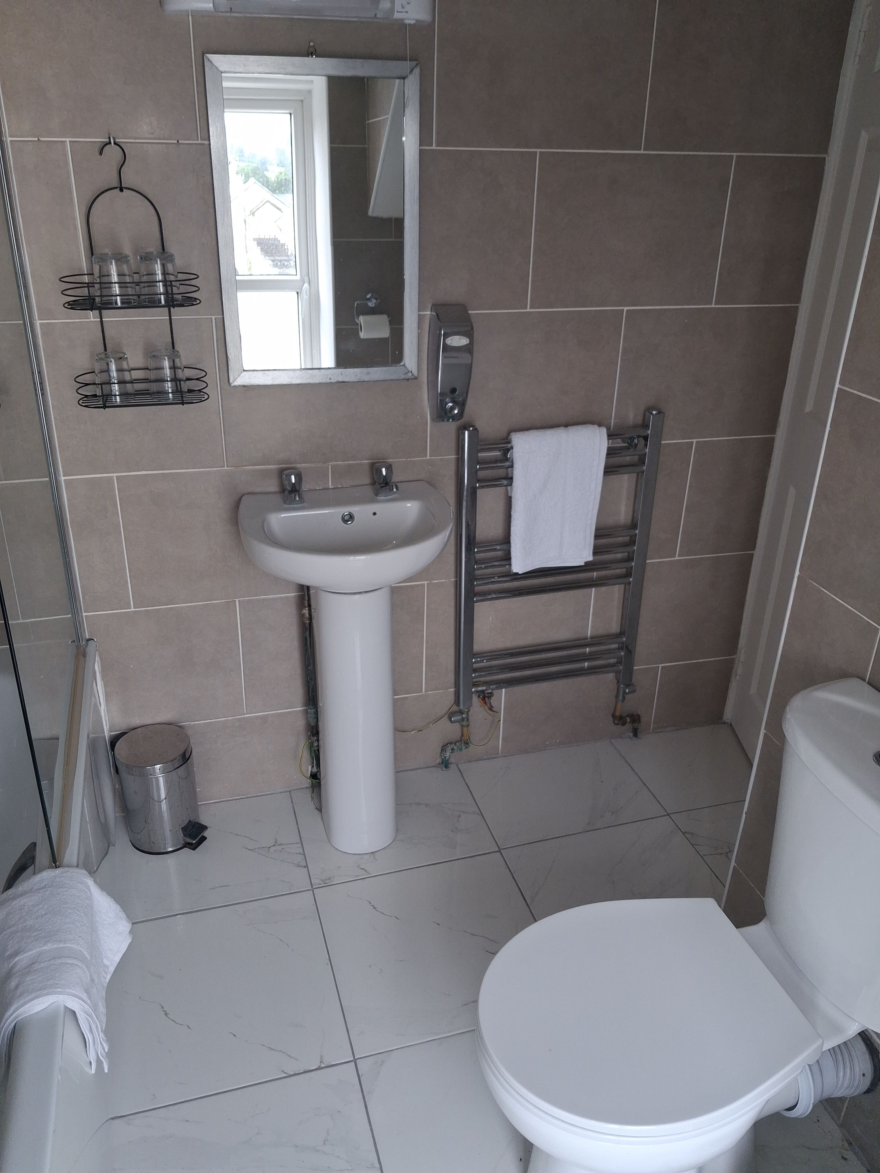 Un baño con lavamanos blanco, inodoro, toallero y cubo de basura metálico.