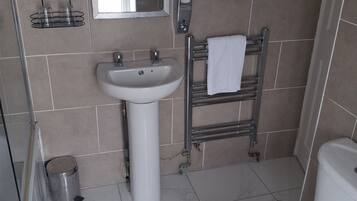 Un baño con lavamanos blanco, inodoro, toallero y cubo de basura metálico.
