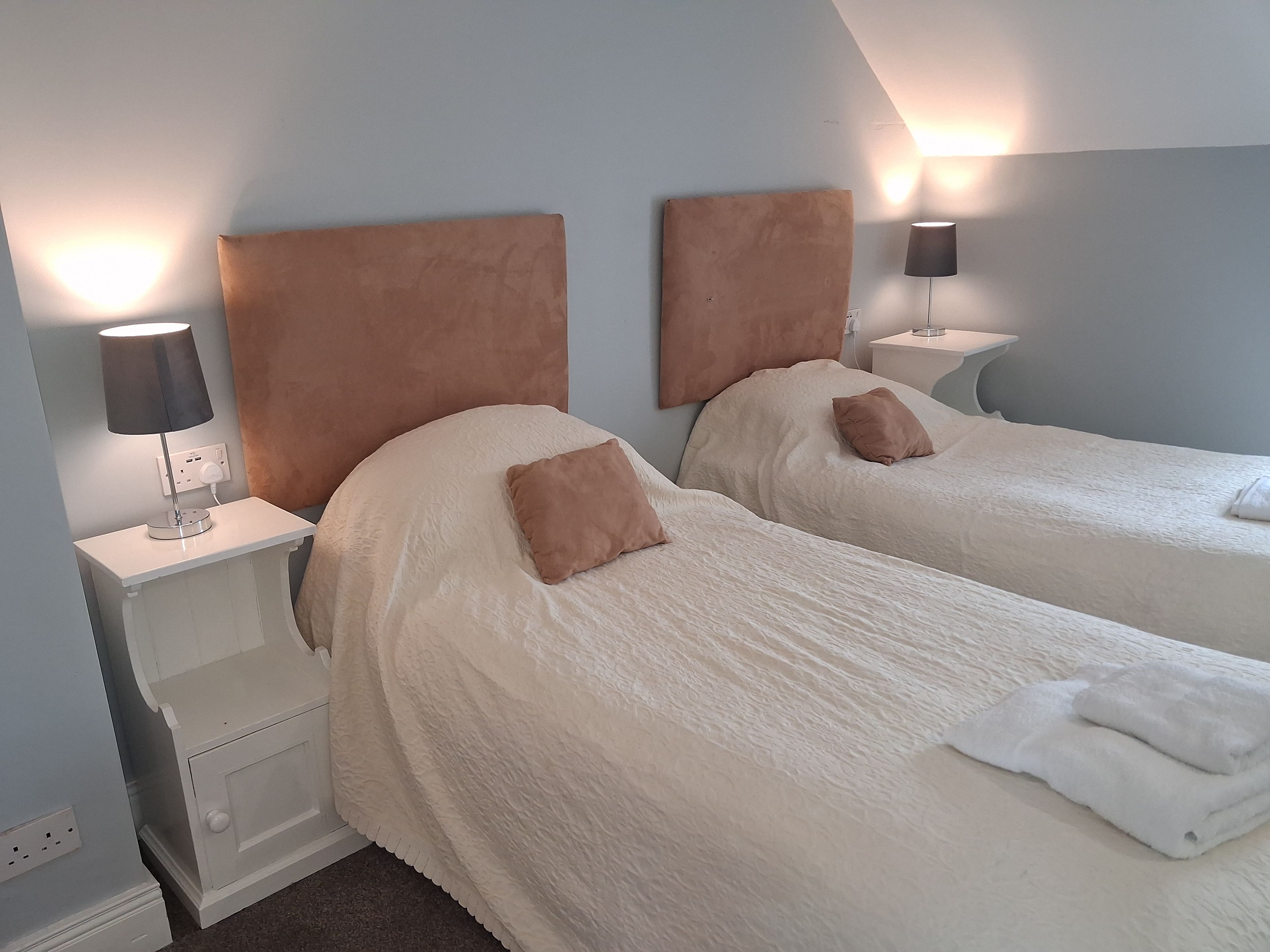 Et hotelværelse med to senge, hver med sengegavl, sengeborde med lamper.