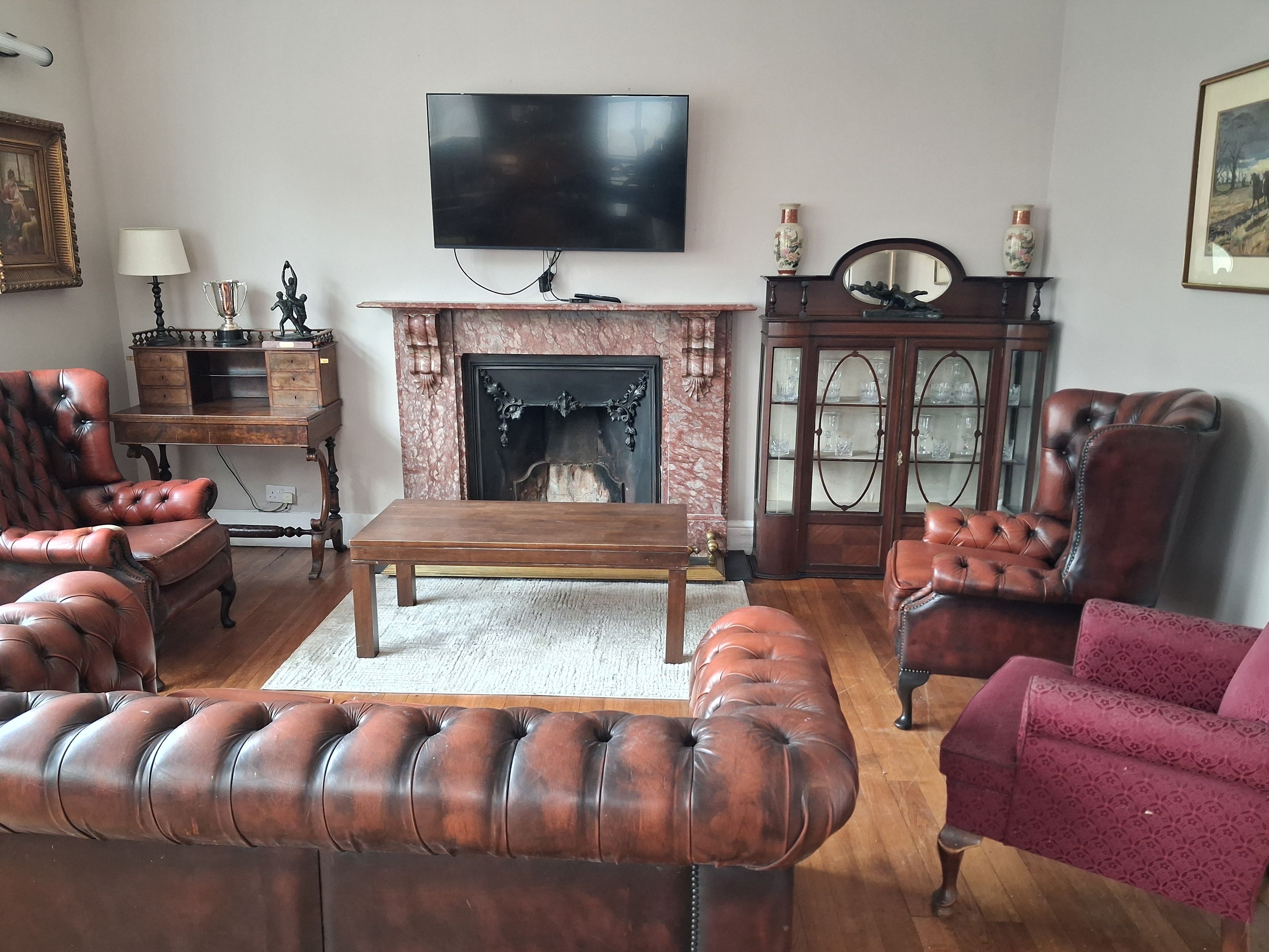 Una sala de estar con sillones de cuero, una mesa de centro de madera, una chimenea, un televisor y un mueble con puertas de vidrio.