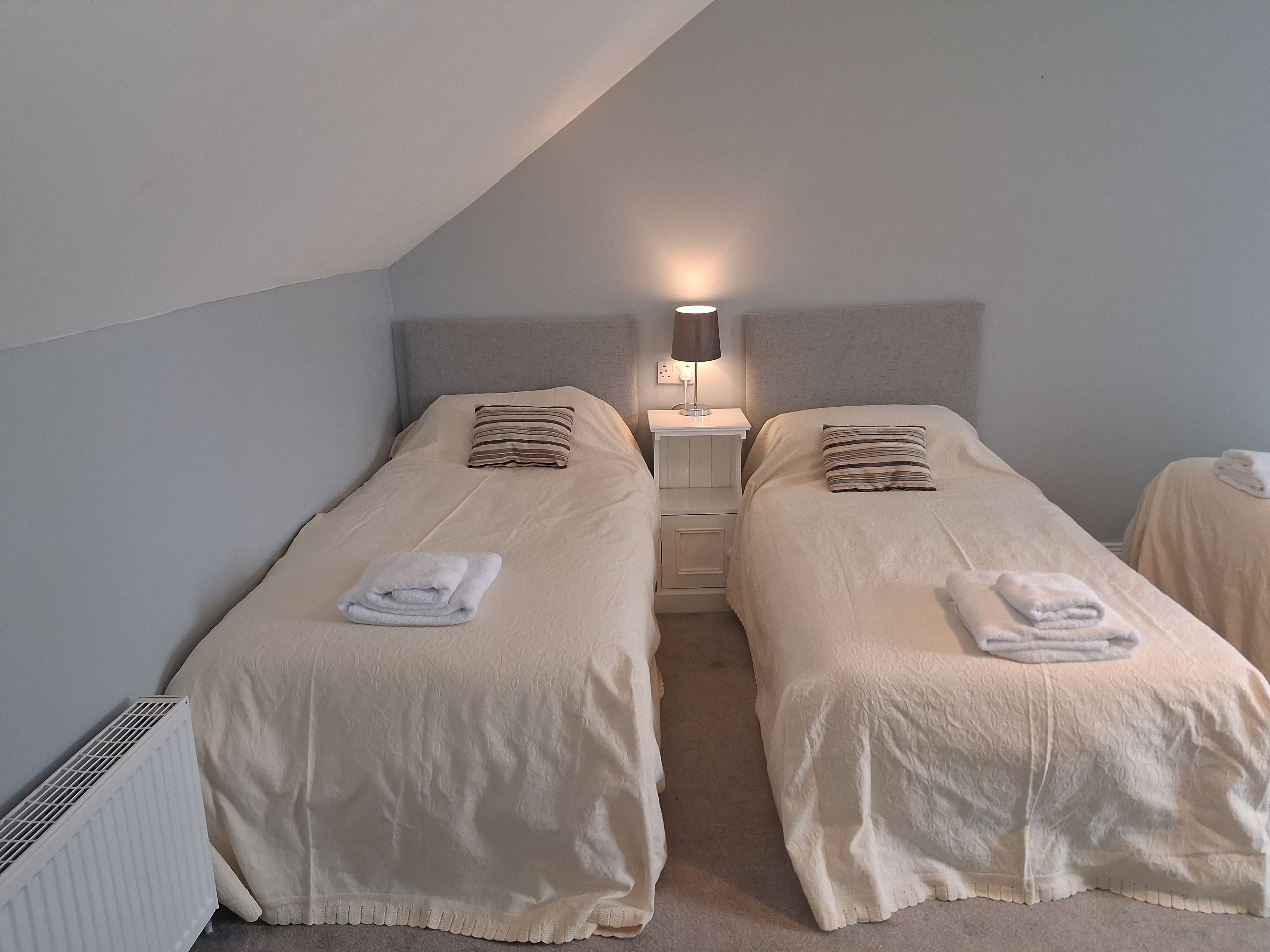 Een tweepersoonskamer met twee bedden, een nachtkastje met lamp en een radiator.