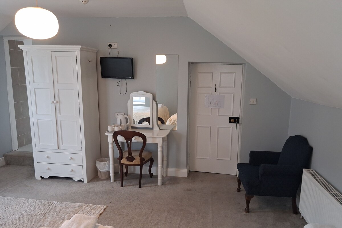 A room with a white desk, a chair, a wardrobe, a television, and a door.