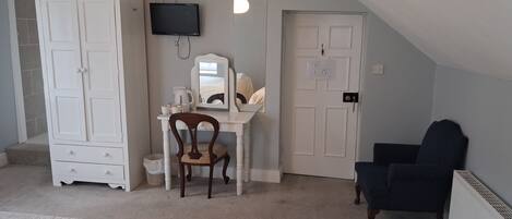 Una habitación con un escritorio blanco, una silla, un armario, un televisor y una puerta.
