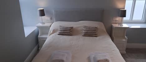 A neatly made bed with pillows and folded towels, a bedside table with a lamp, and a window with a view.
