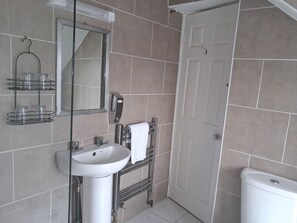Un baño con lavamanos blanco, espejo, toallero y retrete blanco.