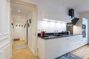 A modern kitchen with white cabinetry, a black countertop, and a stainless steel range hood. - L'Appart June - 4 Guests - In the Heart of Town (Gérardmer)