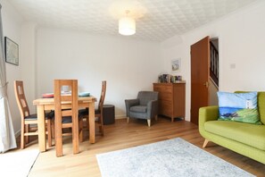 Ein Zimmer mit Esstisch, Stühlen, einer Couch, einer Lampe und einem Bild an der Wand.