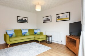 Ein Wohnzimmer mit einem grünen Sofa, einem Fernseher auf einem Holzboden und drei gerahmten Bildern an der Wand.