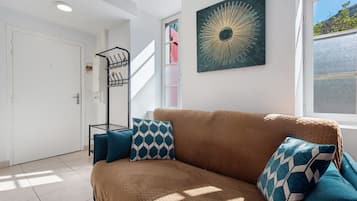 Ein modernes Wohnzimmer mit einer braunen Couch, gemusterten Kissen, einem Wandbild und einem Fenster mit Aussicht.