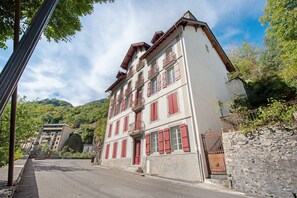 A multi-story building with a stone facade, red shutters, and a balcony with wrought iron railings. - Le Refuge de l’Impératrice Apartment with Mountain View and Wi-Fi (Luz-Saint-Sauveur)