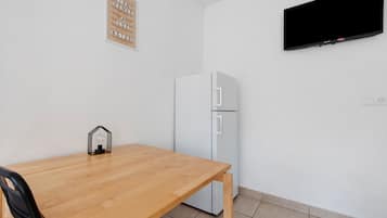Una habitación con una mesa de madera, un refrigerador blanco, un televisor montado y un letrero con texto.