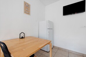 A room with a wooden table, a white refrigerator, a mounted television, and a sign with text. - Le Refuge de l’Impératrice Apartment with Mountain View and Wi-Fi (Luz-Saint-Sauveur)